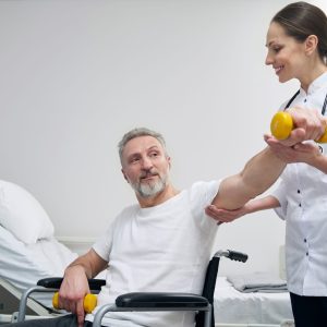 Concentrated disabled person lifting dumbbell supported by physiotherapist