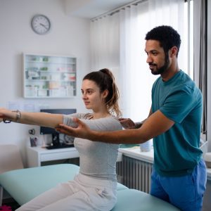 Young male physiotherapist examining young woman patient in a physic room